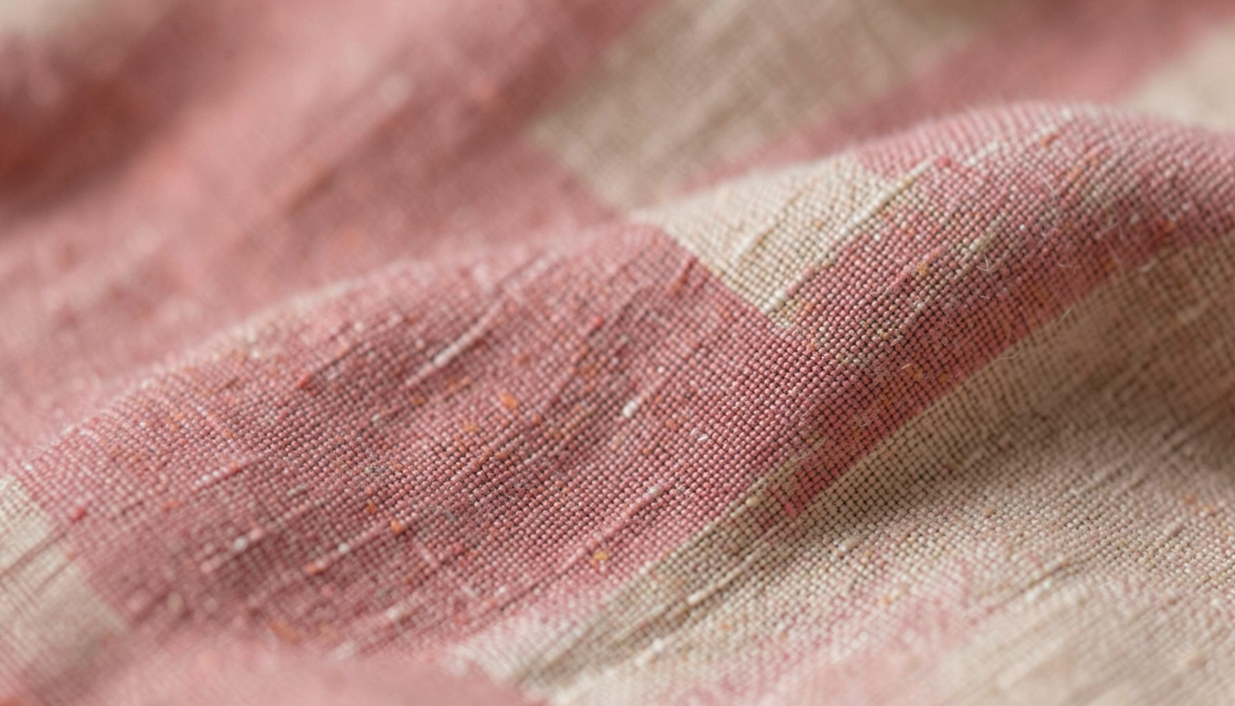 Soft abstract texture of brushed linen fabric in muted dusty rose and sandy beige tones, warm and tactile